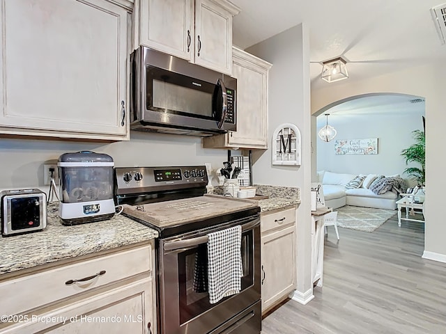 kitchen with light wood-type flooring, light stone counters, arched walkways, appliances with stainless steel finishes, and baseboards