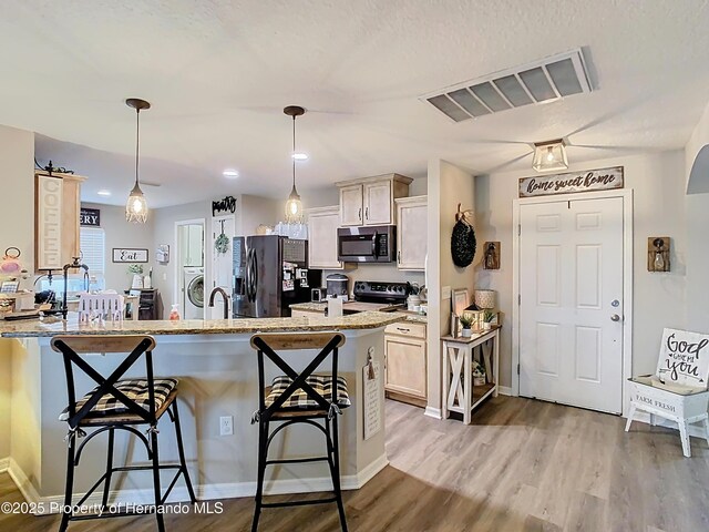 kitchen with visible vents, a breakfast bar, electric stove, stainless steel microwave, and black refrigerator with ice dispenser