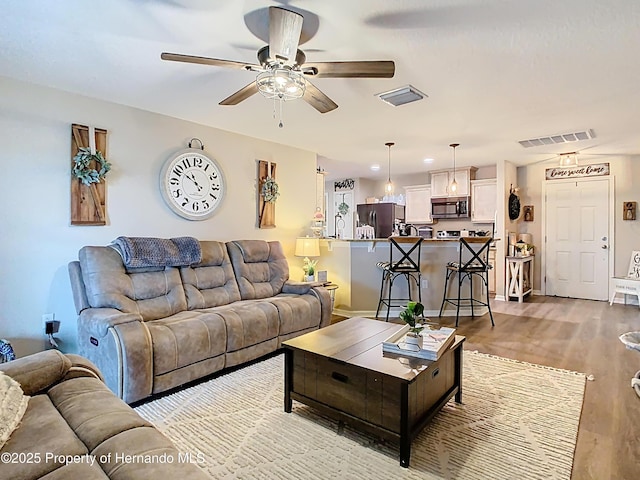 living room with visible vents, baseboards, light wood-style floors, and ceiling fan