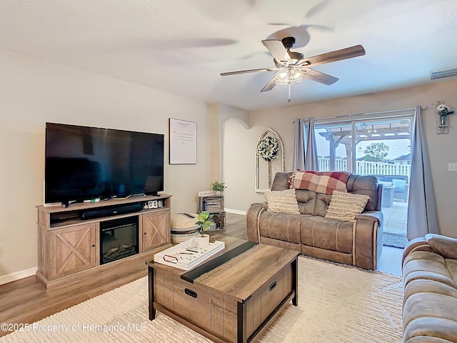 living room featuring ceiling fan, visible vents, baseboards, and wood finished floors