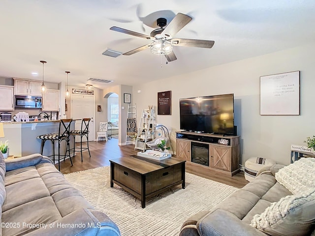 living room featuring visible vents, light wood-style flooring, a ceiling fan, and arched walkways