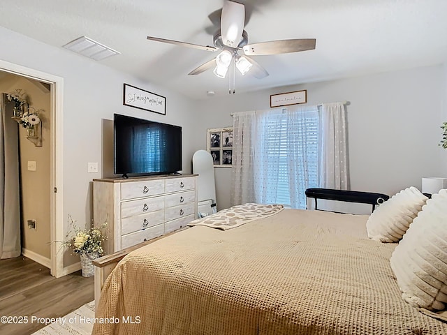 bedroom featuring ceiling fan, visible vents, baseboards, and wood finished floors