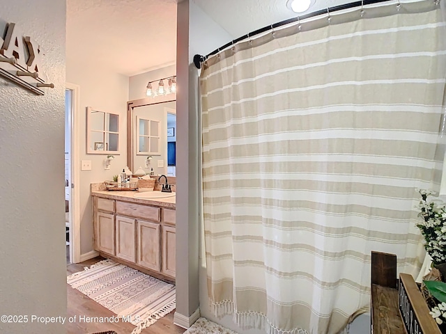 full bath with vanity, a shower with shower curtain, wood finished floors, baseboards, and a textured wall