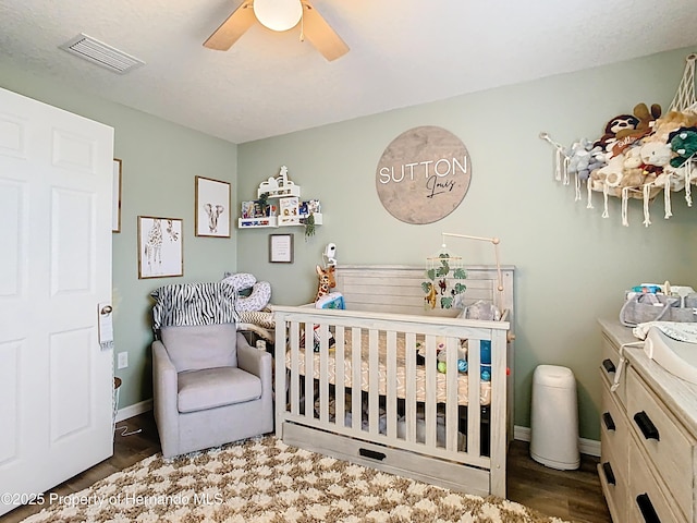 bedroom with a ceiling fan, wood finished floors, baseboards, visible vents, and a nursery area