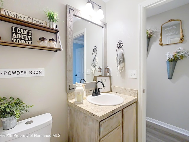 half bath with toilet, vanity, baseboards, and wood finished floors