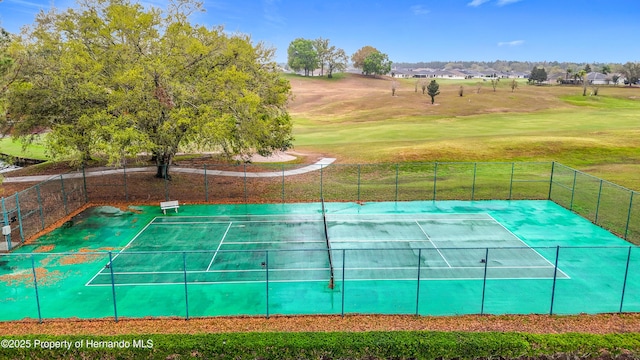 view of tennis court featuring a lawn and fence