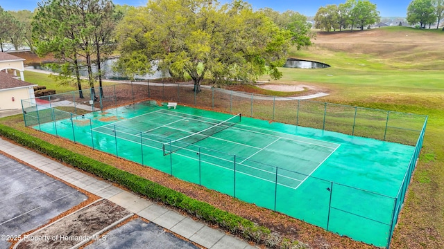 view of tennis court with a water view, a lawn, and fence