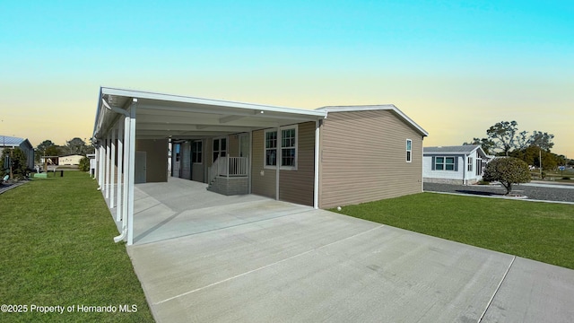 property exterior at dusk featuring an attached carport, concrete driveway, and a yard