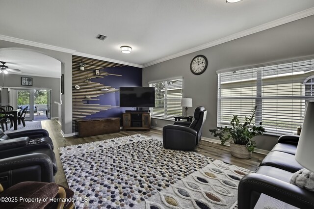 living area with arched walkways, visible vents, crown molding, and wood finished floors