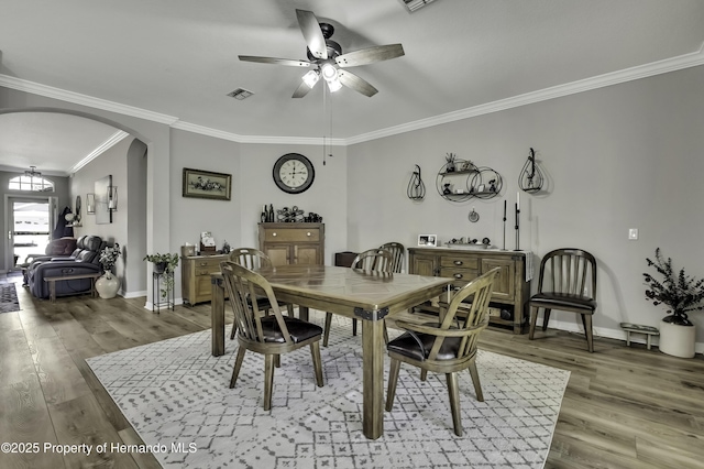 dining room featuring light wood-style flooring, baseboards, arched walkways, and ornamental molding