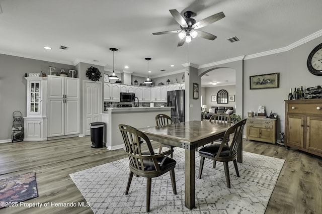 dining room with light wood-style floors, visible vents, and arched walkways