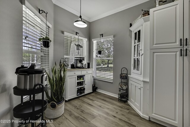 kitchen with glass insert cabinets, crown molding, baseboards, light wood-style flooring, and white cabinets