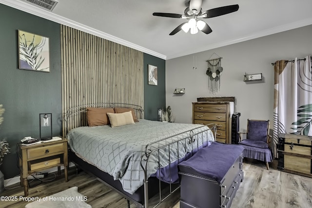 bedroom with visible vents, wood finished floors, a ceiling fan, and ornamental molding