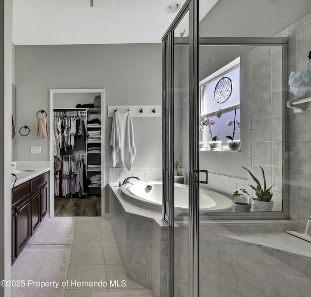 full bathroom featuring a walk in closet, a shower stall, a bath, and tile patterned flooring