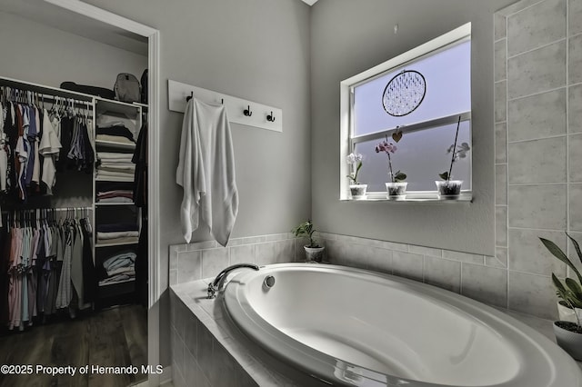 full bath featuring a garden tub, a spacious closet, and wood finished floors