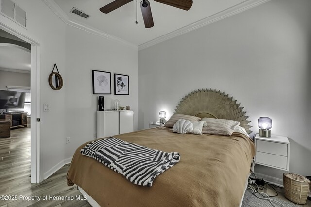 bedroom featuring arched walkways, wood finished floors, visible vents, and ornamental molding