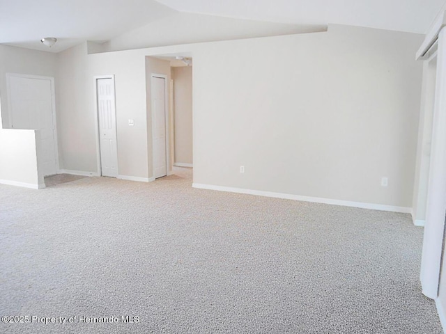 spare room with lofted ceiling, light colored carpet, and baseboards