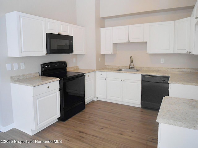 kitchen featuring black appliances, a sink, wood finished floors, white cabinets, and light countertops