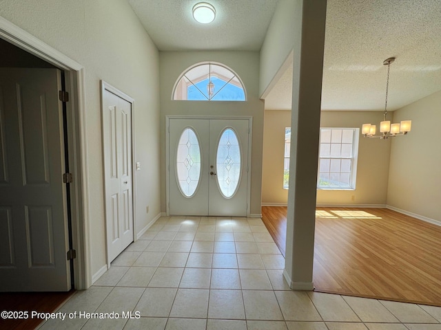 foyer entrance featuring light tile patterned floors, baseboards, a textured ceiling, and an inviting chandelier