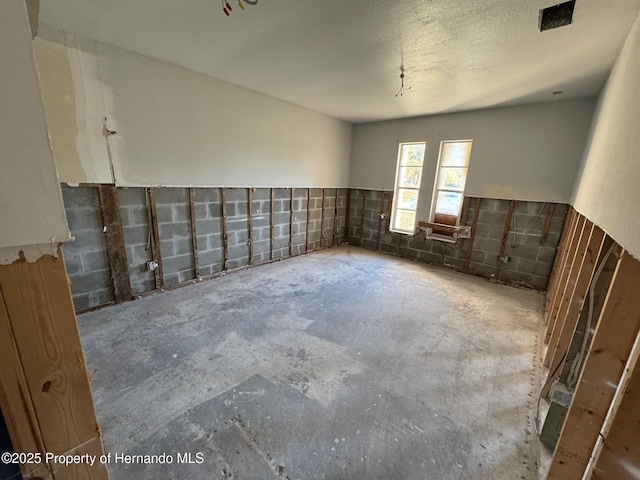 unfurnished room featuring unfinished concrete floors, concrete block wall, and a textured ceiling