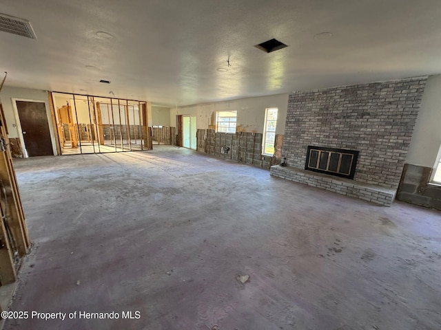 unfurnished living room with visible vents, a brick fireplace, and unfinished concrete flooring