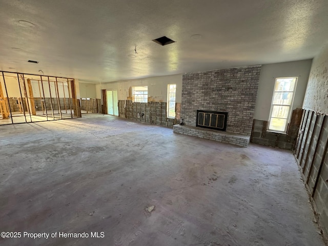 unfurnished living room with a textured ceiling, a fireplace, concrete flooring, and a healthy amount of sunlight