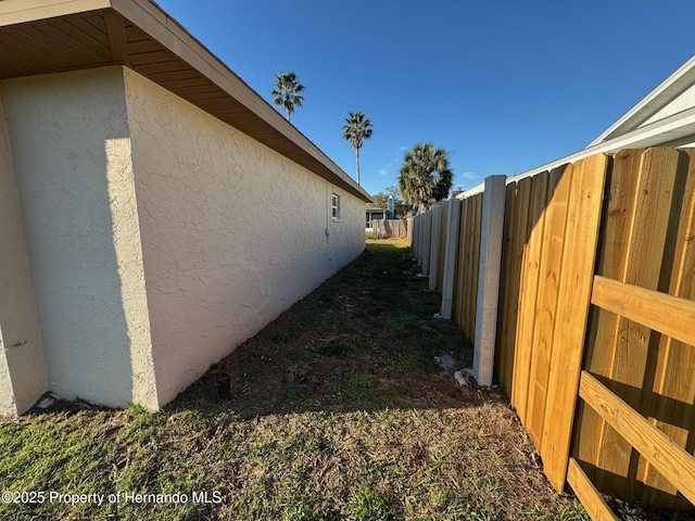 view of side of home with stucco siding and fence