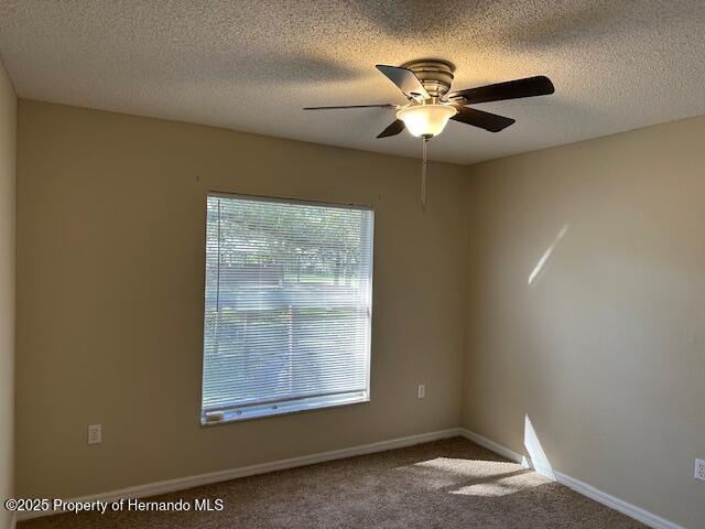 carpeted spare room with a textured ceiling, baseboards, and ceiling fan