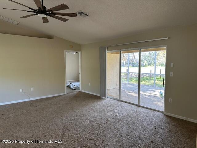 carpeted empty room featuring visible vents, a textured ceiling, baseboards, and vaulted ceiling