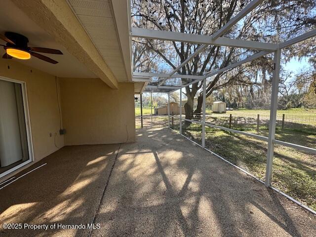 view of patio featuring fence, ceiling fan, an outdoor structure, a storage shed, and a lanai