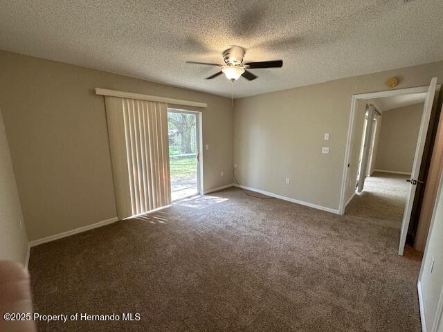 empty room with a textured ceiling, carpet flooring, baseboards, and ceiling fan