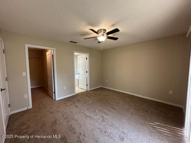 unfurnished bedroom featuring a spacious closet, visible vents, baseboards, carpet flooring, and a textured ceiling