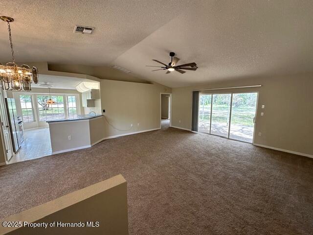 unfurnished living room with visible vents, ceiling fan with notable chandelier, a textured ceiling, dark carpet, and lofted ceiling