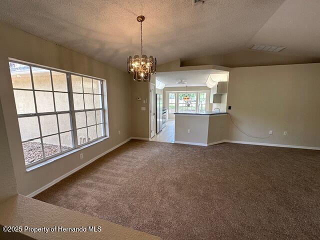 carpeted empty room with baseboards, a textured ceiling, an inviting chandelier, and vaulted ceiling