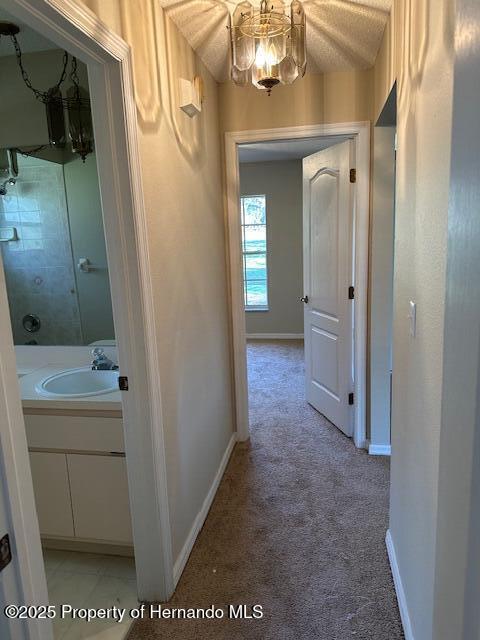 hall featuring light colored carpet, baseboards, and a sink