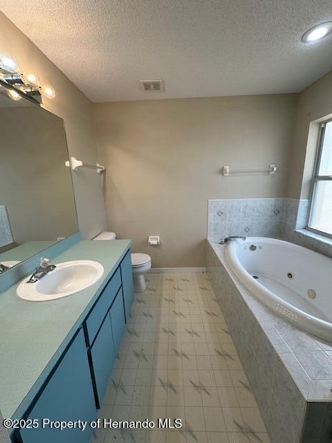 full bath with visible vents, toilet, vanity, a tub with jets, and a textured ceiling