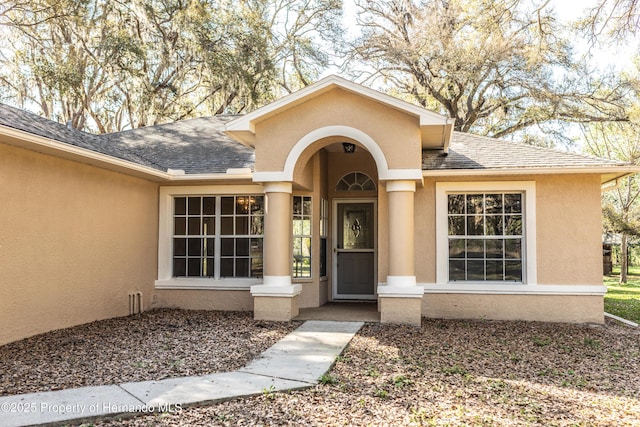 doorway to property featuring roof with shingles and stucco siding