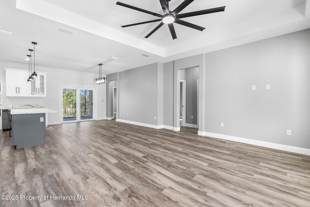 unfurnished living room featuring visible vents, ceiling fan with notable chandelier, baseboards, and wood finished floors