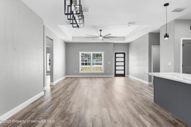 unfurnished living room with a raised ceiling, wood finished floors, and baseboards