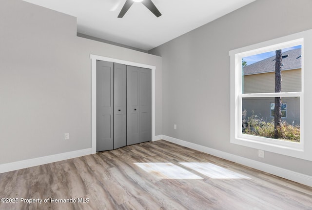 unfurnished bedroom with a closet, multiple windows, baseboards, and wood finished floors