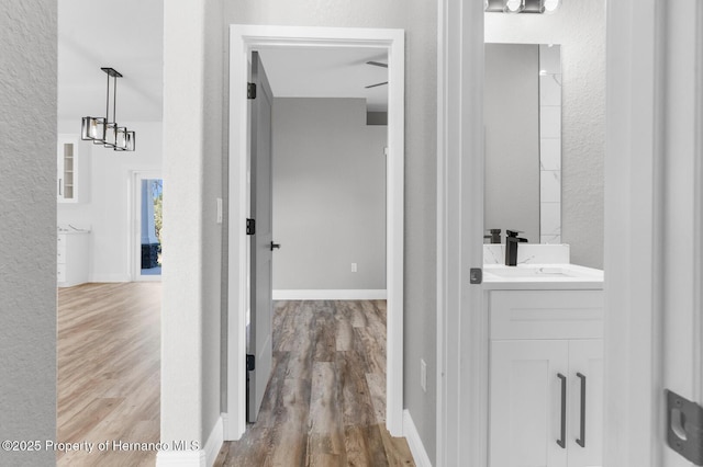 hall featuring a textured wall, wood finished floors, baseboards, and a sink