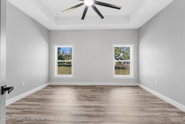 unfurnished room featuring ceiling fan, baseboards, a raised ceiling, and wood finished floors