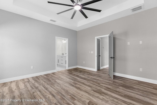 unfurnished bedroom with visible vents, a raised ceiling, baseboards, and wood finished floors