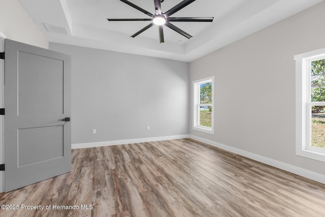 empty room with baseboards, a raised ceiling, and plenty of natural light