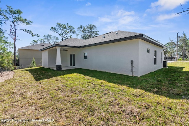 rear view of property with central AC unit, a lawn, a ceiling fan, and stucco siding