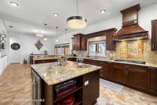 kitchen featuring wine cooler, a center island with sink, stainless steel gas stovetop, custom exhaust hood, and a sink