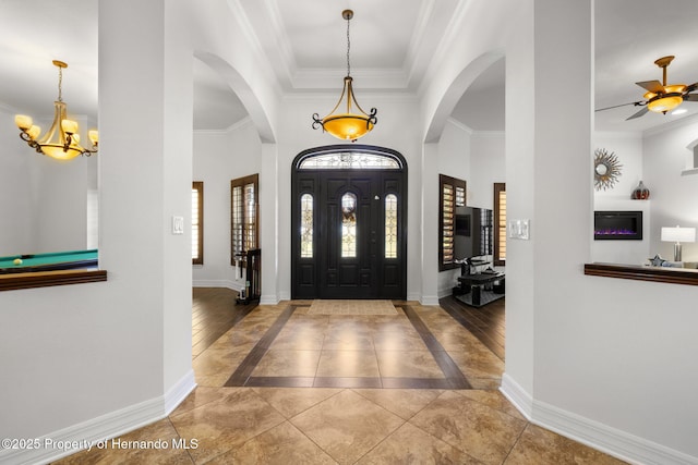 entryway featuring arched walkways, ceiling fan with notable chandelier, baseboards, and ornamental molding