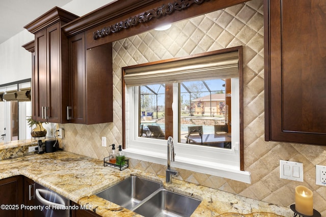 kitchen with dark brown cabinetry, backsplash, light stone countertops, and a sink