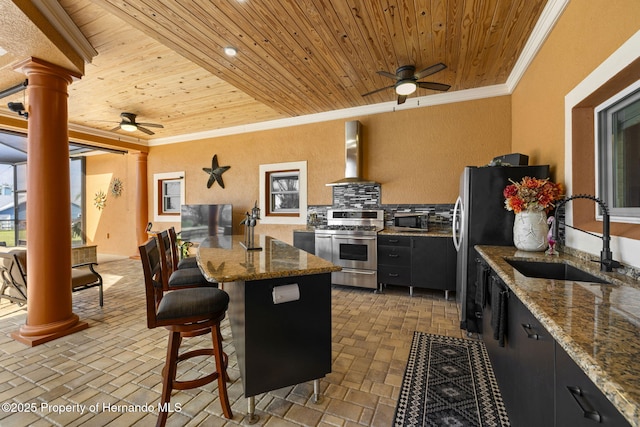 kitchen featuring ornate columns, a sink, ornamental molding, stainless steel appliances, and wall chimney exhaust hood