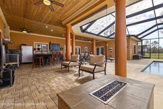 view of patio featuring ceiling fan, glass enclosure, a fire pit, and outdoor dry bar
